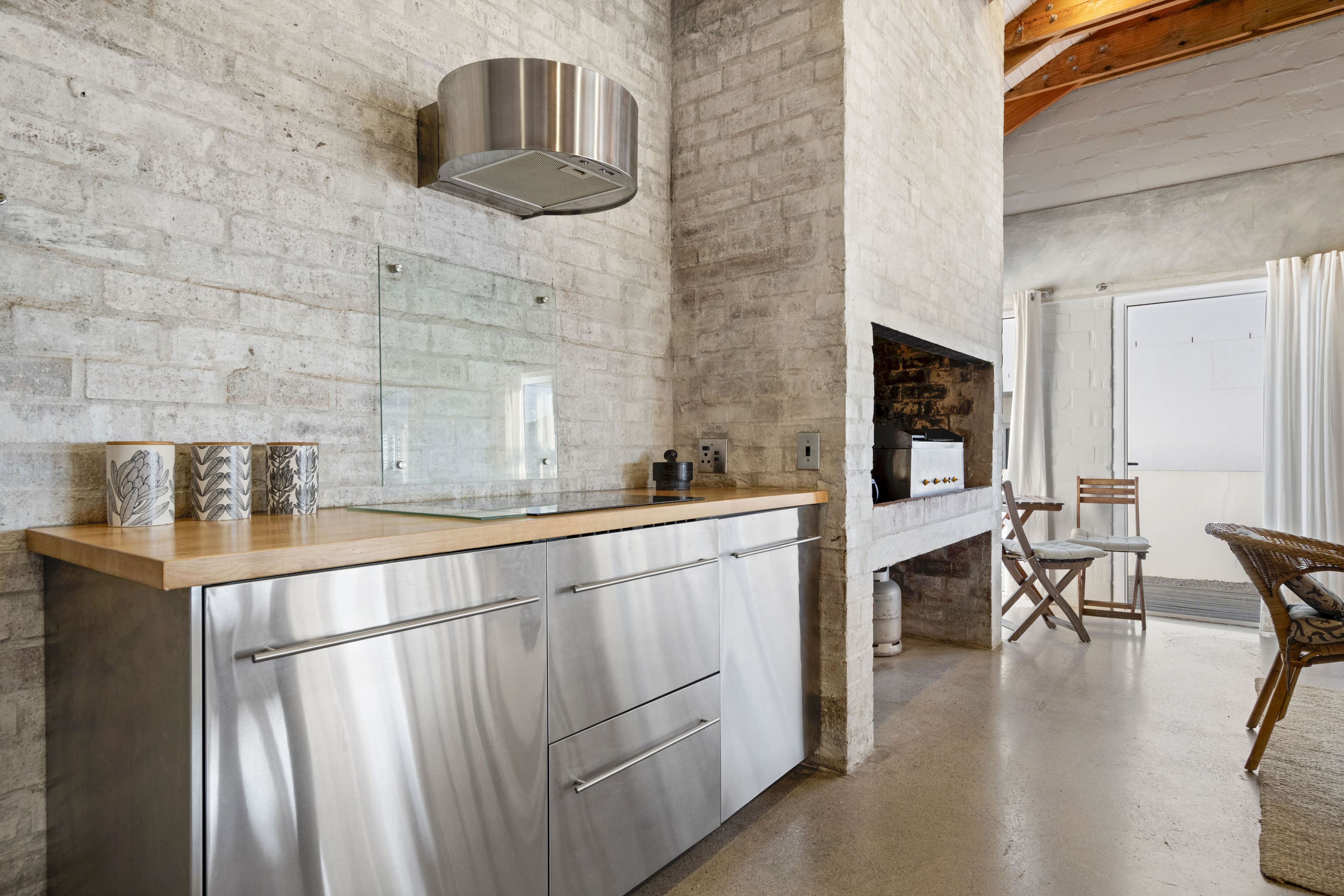 A modern kitchen with stainless steel appliances, a wooden countertop, and a brick wall.