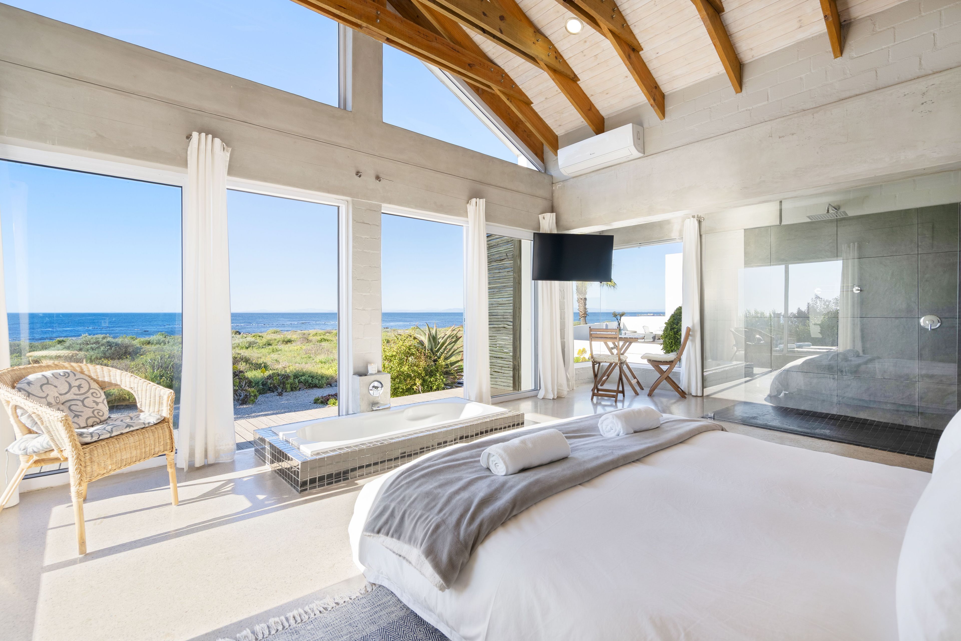 A modern bedroom with a large bed, a TV, and a view of the sea.