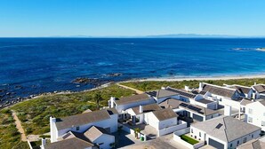 A coastal residential area with houses featuring sloped roofs and solar panels, overlooking a beach and the ocean.