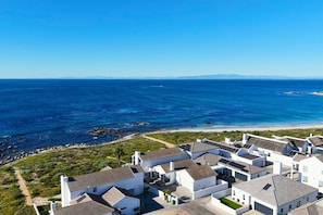 A coastal residential area with houses featuring sloped roofs and solar panels, overlooking a beach and the ocean.