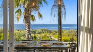 An outdoor dining area with a view of the ocean, equipped with wicker chairs and tables set for two.