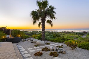A landscaped outdoor area with a palm tree, a wooden deck, and a view of the ocean at sunset.