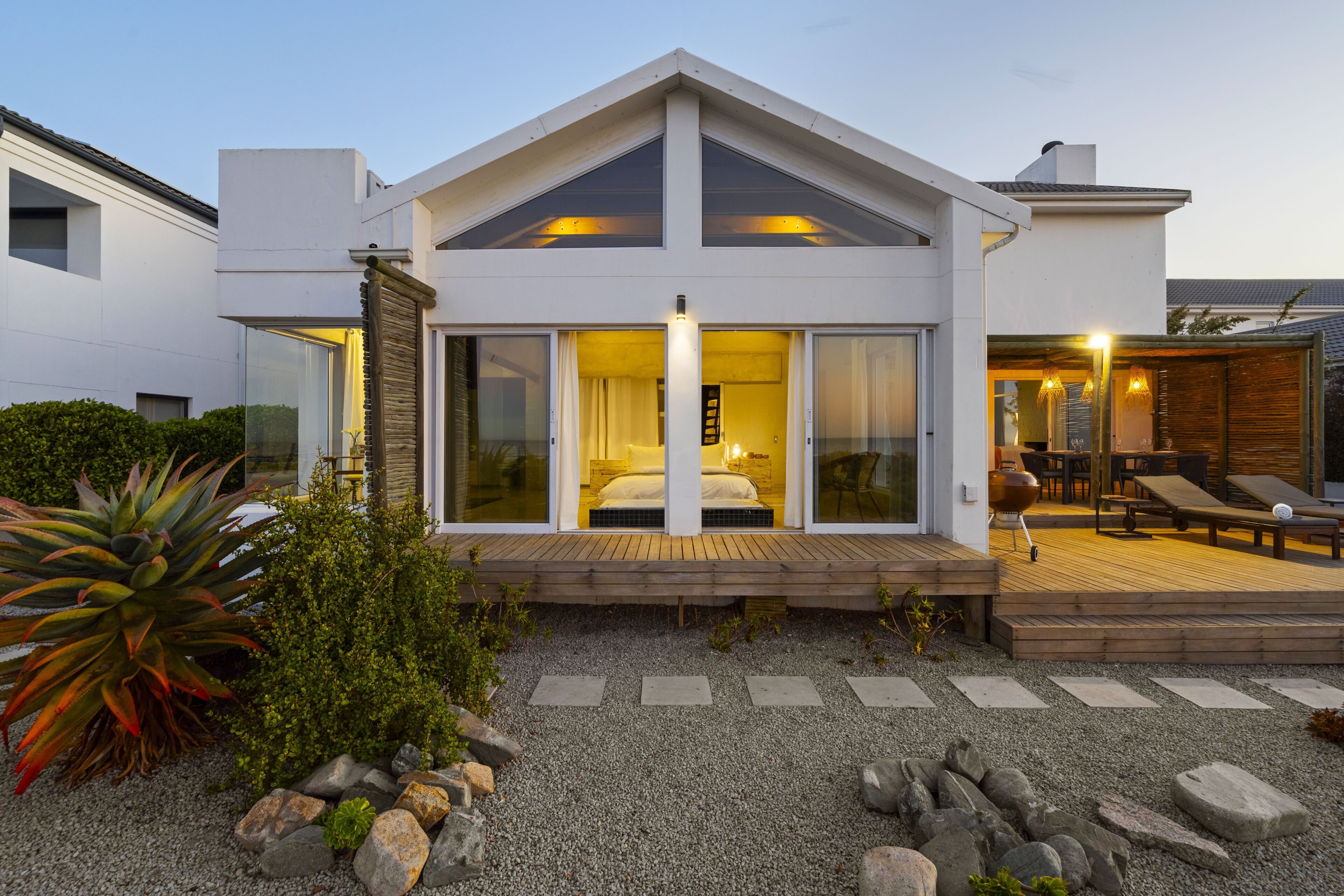 A modern house with a large glass door entrance, a wooden deck, and a patio area with outdoor furniture.