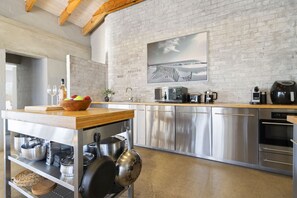 A modern kitchen with stainless steel appliances, a wooden countertop, and a brick wall.
