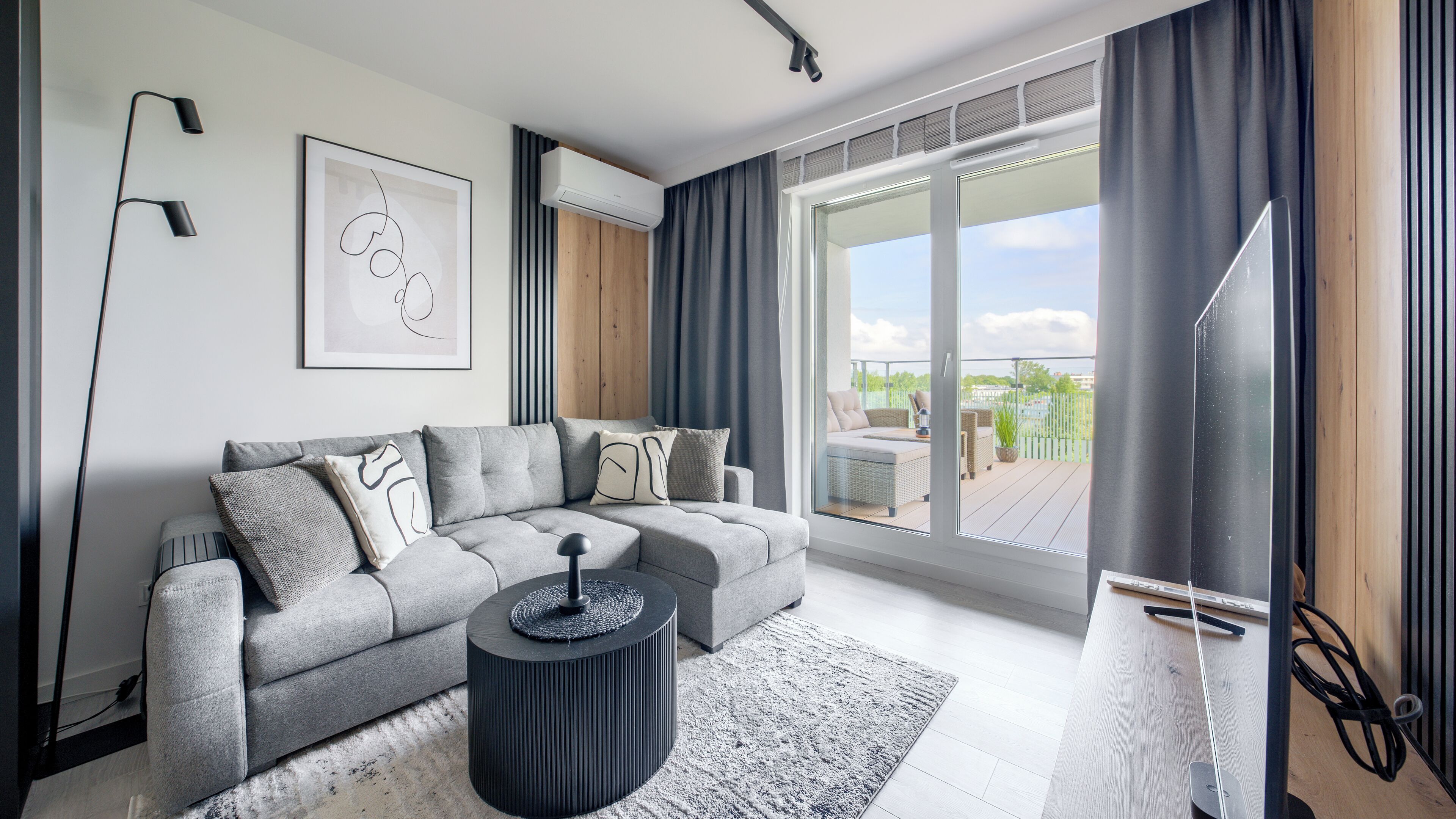 En moderne stue med en hjørnesofa, et rundt sofabord og en stor skydedør til en udendørs terrasse.