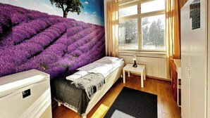 A bedroom with a bed, a nightstand, a window with curtains, and a wall mural of a purple field.