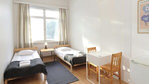 Una habitación con dos camas, un escritorio, una silla, un radiador y una ventana con cortinas.