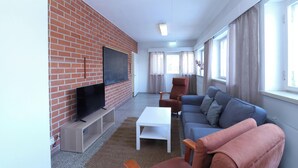 Una sala de estar con pared de ladrillo, un televisor de pantalla plana, un sofá, una mesa de centro y una ventana con cortinas.