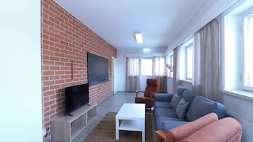 Olohuone, jossa on tiiliseinä, litteänäyttöinen televisio, sohva, sohvapöytä ja ikkuna, jossa on verhot.