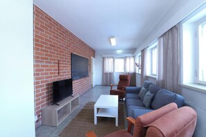A living room with a brick wall, a flat-screen TV, a sofa, a coffee table, and a window with curtains.