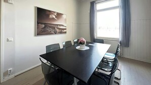 Un salón de conferencias con una mesa grande, sillas, un cuadro en la pared y una ventana con cortinas.