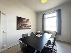 A conference room with a large table, chairs, a wall-mounted painting, and a window with curtains.