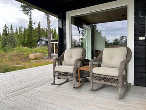Una terraza de madera con dos mecedoras de mimbre y una pequeña mesa.