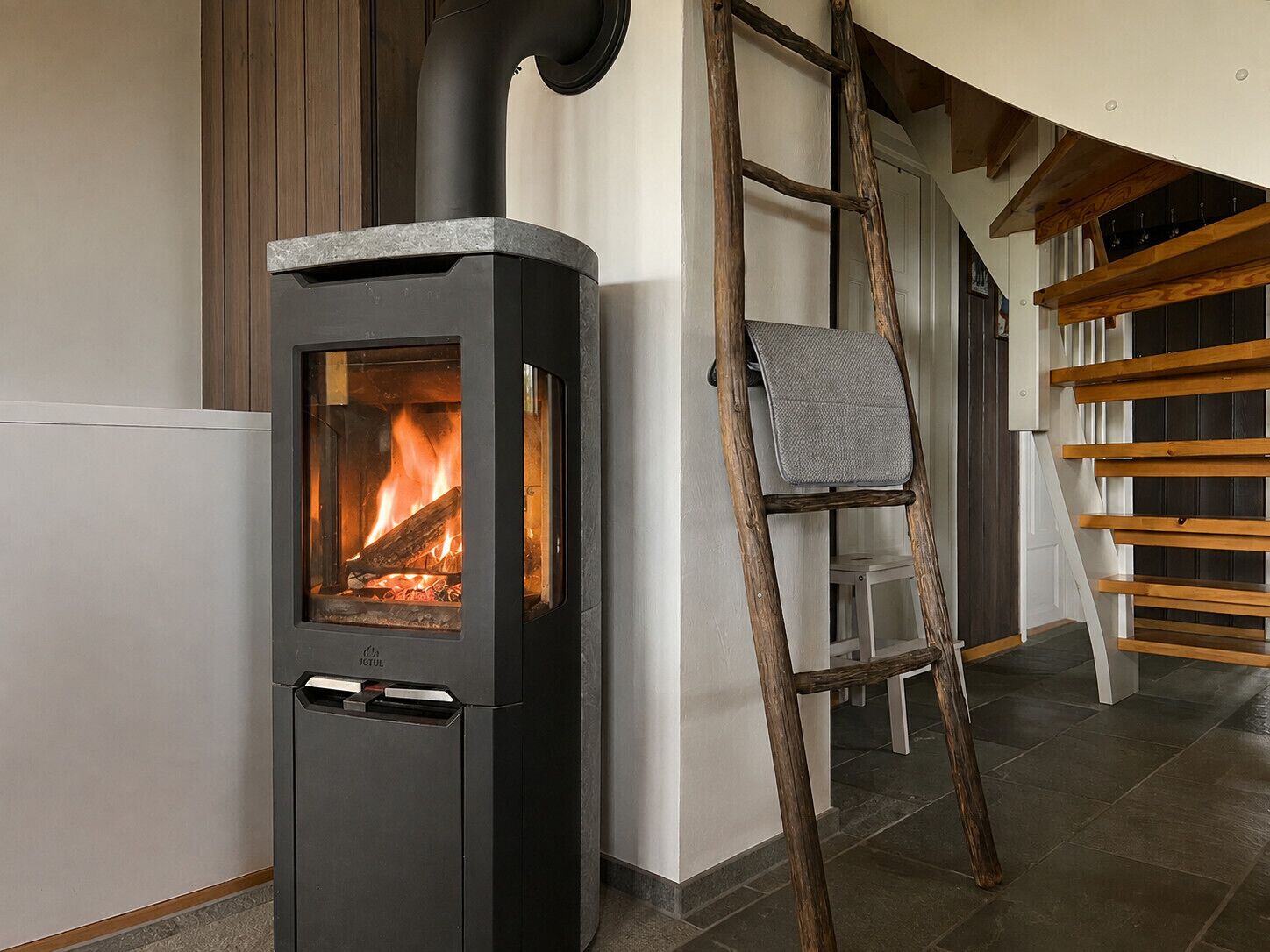 Une cheminée moderne avec un foyer apparent, une échelle en bois et un banc en bois.