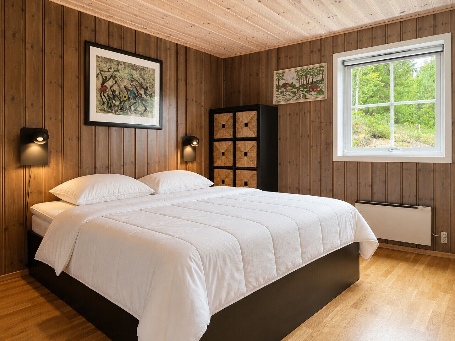 Un dormitorio con una cama, paredes de madera, una ventana y dos lámparas fijadas a la pared.