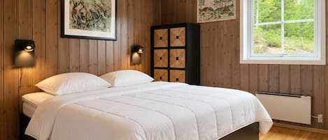 A bedroom with a bed, wooden walls, a window, and two wall-mounted light fixtures.