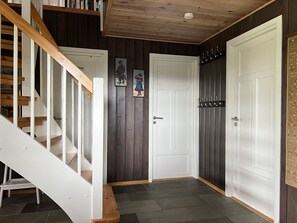 Una escala que condueix a una habitació amb una porta blanca, un penjador i una petita banca.