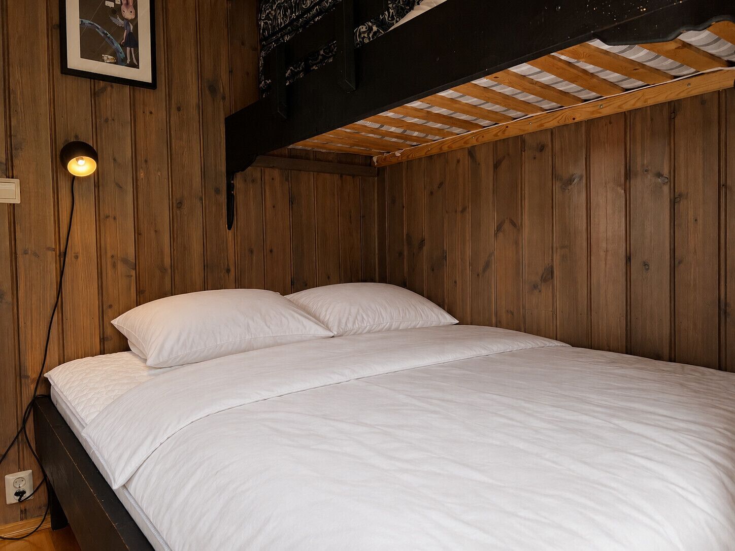 En enkeltseng med hvide sengetæger i et rum med trævægge og et skråt loft.