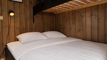En enkeltseng med hvide sengetæger i et rum med trævægge og et skråt loft.