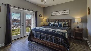 A bedroom with a large bed, a ceiling fan, a window with curtains, and a wall sign.