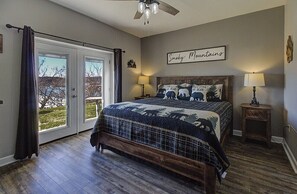 A bedroom with a large bed, a ceiling fan, a window with curtains, and a wall sign. -         MOUNTAIN VIEW BLESSINGS VIEW SERENITY of MTS. Newly Remodeled 2Bed2Bath (Pigeon Forge)