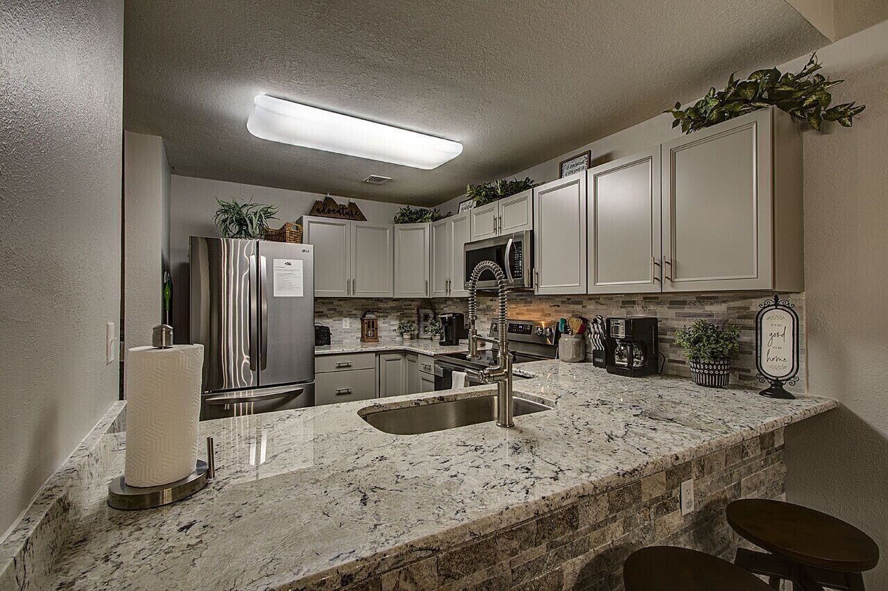 A kitchen with white cabinets, a stainless steel refrigerator, a granite countertop, and a built-in microwave.
