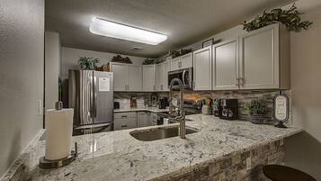 A kitchen with white cabinets, a stainless steel refrigerator, a granite countertop, and a built-in microwave.