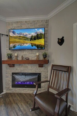 A living room with a stone fireplace, a mounted television, and a mounted bear head decoration. -         MOUNTAIN VIEW BLESSINGS VIEW SERENITY of MTS. Newly Remodeled 2Bed2Bath (Pigeon Forge)