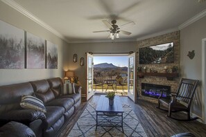 A living room with a leather sofa, a coffee table, a fireplace, and a view of a mountainous landscape through an open door.