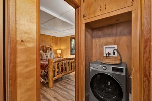 A room with a bed, a washing machine, and wooden cabinets. - New Listing Big Bear Lake 2BR/1BA | Fireplace & Deck (Big Bear Lake)