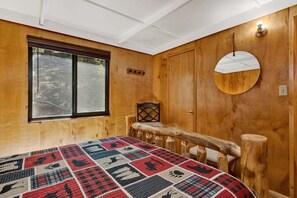 A room with a large window, a wooden door, a round mirror, and a bed with a patterned quilt. - New Listing Big Bear Lake 2BR/1BA | Fireplace & Deck (Big Bear Lake)