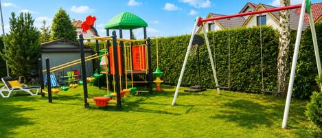 Un parque infantil con una estructura para escalar, columpios y un aro de baloncesto.