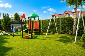 Un parque infantil con una estructura para escalar, columpios y un aro de baloncesto.