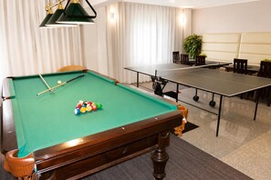 Ein Billardtisch mit Kugeln und Spielstöcken, ein Tischtennis-Tisch und eine Sitzecke mit Stühlen und Tisch.
