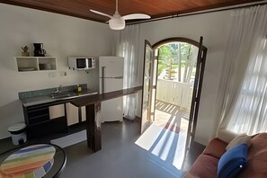 Ein kompakter Wohnbereich mit Küchenzeile, Essplatz und Blick auf einen Garten durch einen Durchgang.