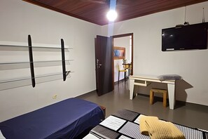 Ein Zimmer mit einem Bett, einem Schreibtisch, einem Sessel und einem Fernseher.