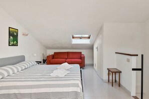 Une chambre à coucher avec un lit, un canapé rouge, une petite table et une lucarne.