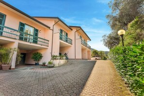 A building with a paved driveway, outdoor plants, and a vehicle parked in front. - [RoadToTheSea]Lerici/Private parking /terrace (Lerici)