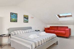Ein Schlafzimmer mit einem Bett, einem roten Sofa, einem Oberlicht und zwei Wandbildern.