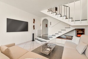 Un salon moderne avec un canapé, une table basse, un téléviseur et un escalier.