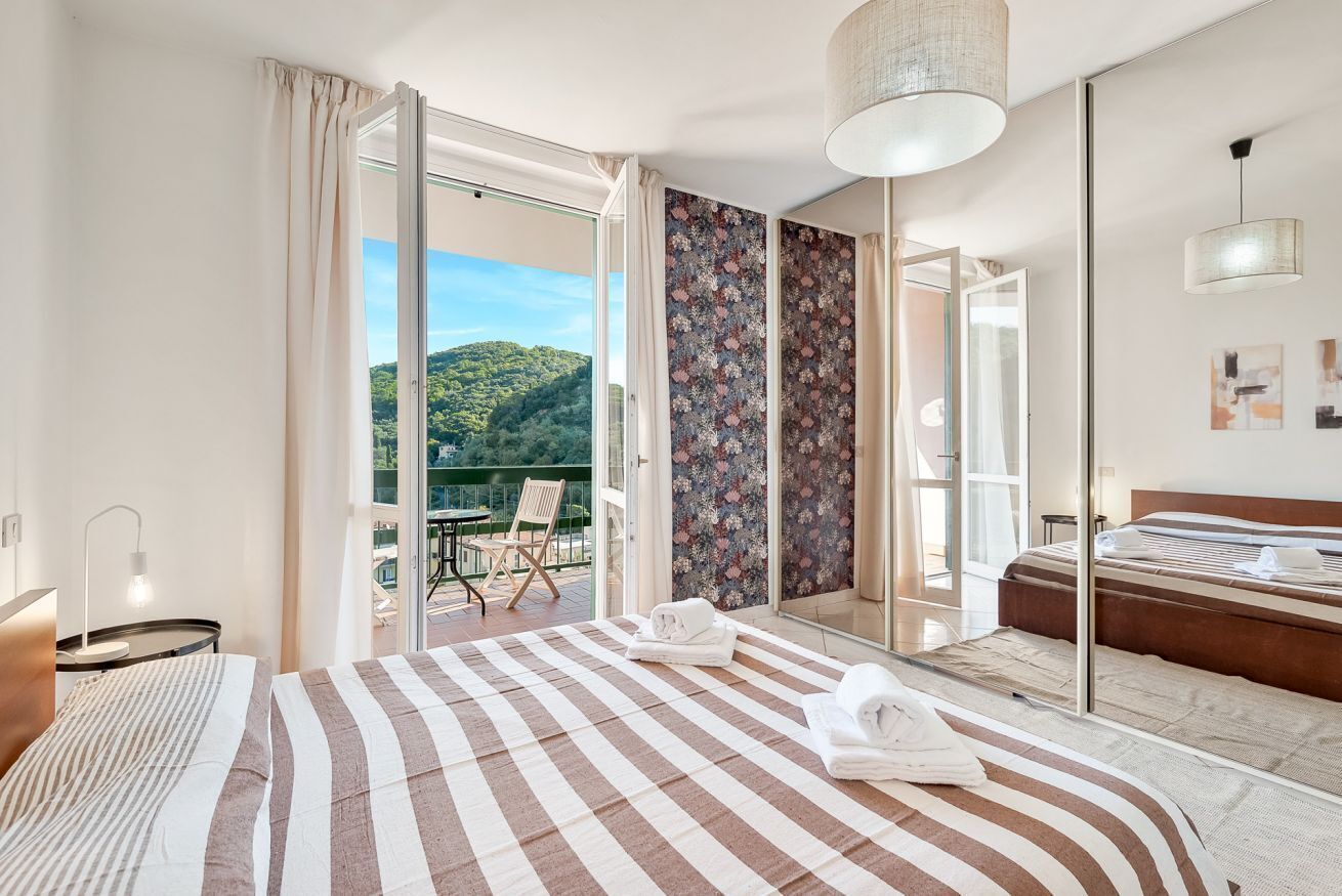 Ein Hotelzimmer mit Bett, einem Balkon mit Blick auf Grünflächen, einem großen Spiegel und einer hängenden Leuchte.