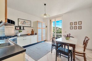 A modern kitchen with white cabinets, a gas stove, and a dining area with a table and chairs. - [RoadToTheSea]Lerici/Private parking /terrace (Lerici)
