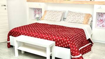 Een bed met een rood beddegoed met patroon, witte kussens en een witte bankje ervoor.