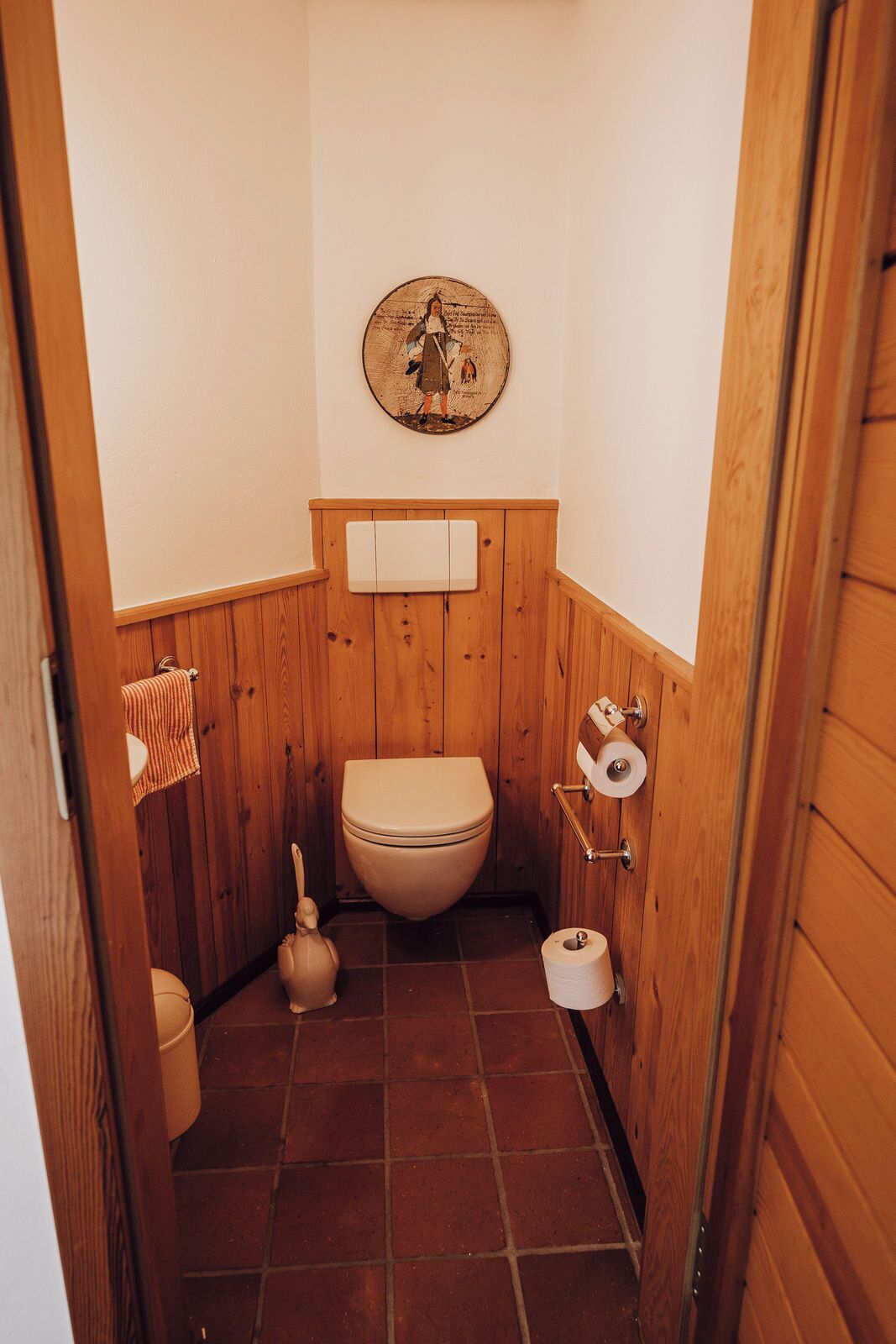 Een kleine badkamer met houten lambrisering, een toilet, een toiletrolhouder en een handdoekrek.