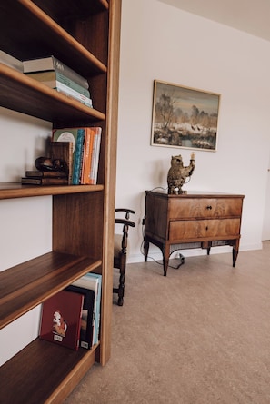 Una habitación con una estantería de madera, un aparador de madera, una silla y un cuadro en la pared.