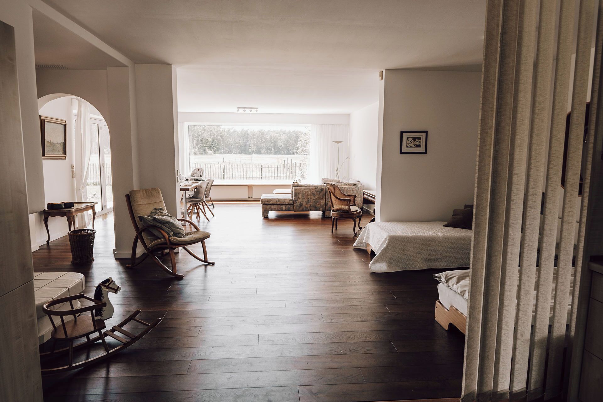 A spacious living room with a dining area, a sofa, a rocking chair, and a bed.