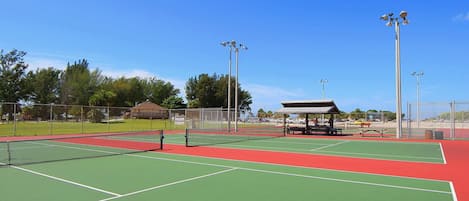 A tennis court with a pavilion, fencing, and trees in the background.