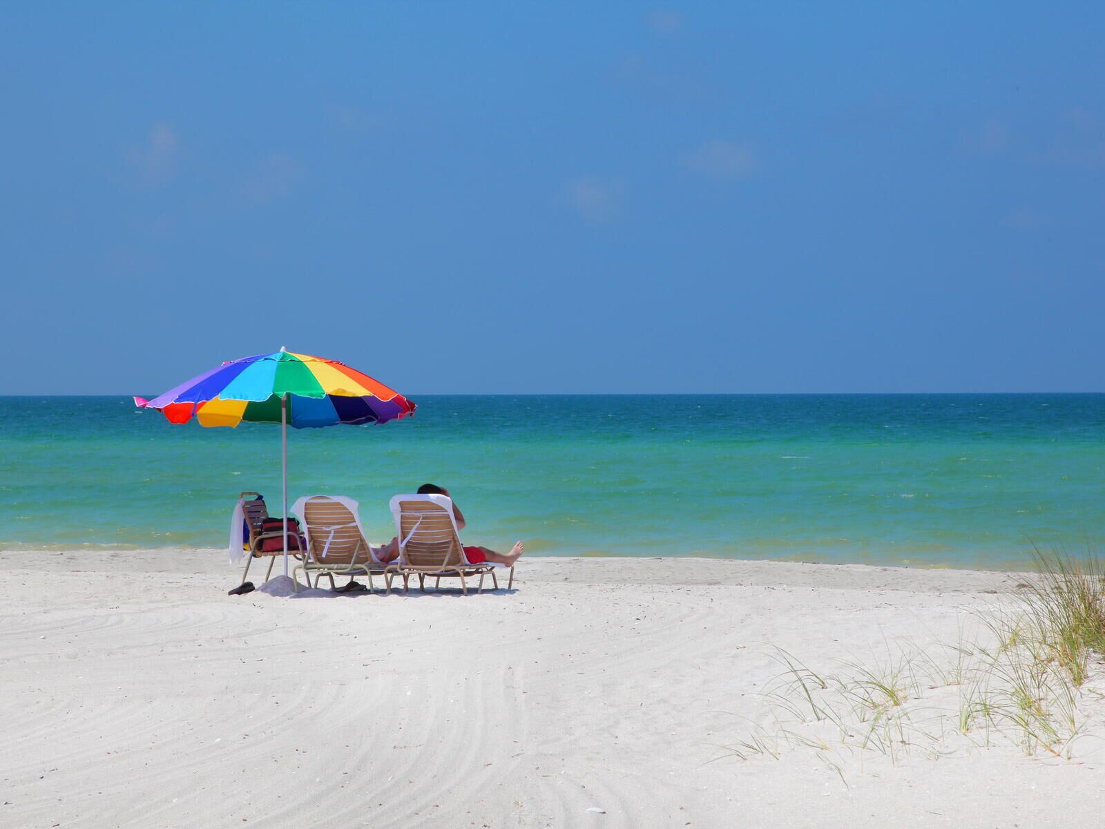 A beach with a colorful umbrella and two lounge chairs facing the ocean.