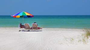Ein Strand mit einem bunten Sonnenschirm und zwei Liegestühlen, die auf den Ozean ausgerichtet sind.