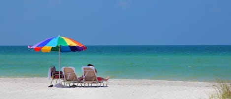 A beach with a colorful umbrella and two lounge chairs facing the ocean.